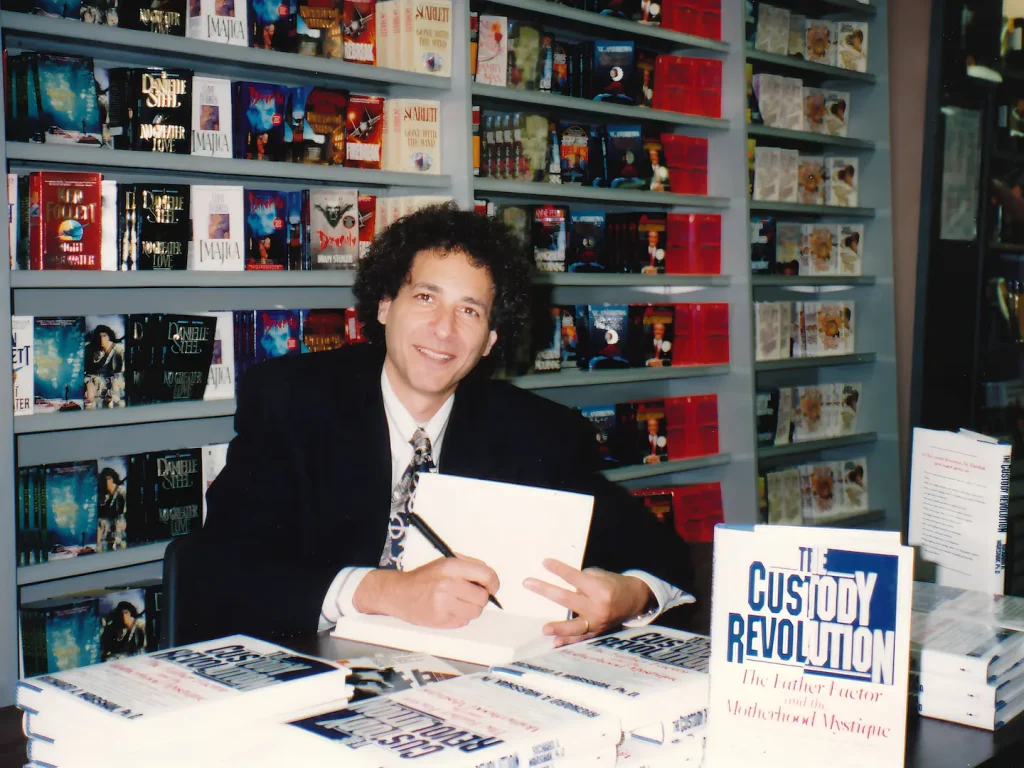 The Custody Revolution author Richard Warshak at a book signing, sat at a desk signing his work for customers